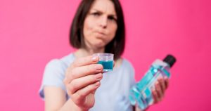 a woman is holding an expired mouthwash bottle while she has a bit of it in her mouth.