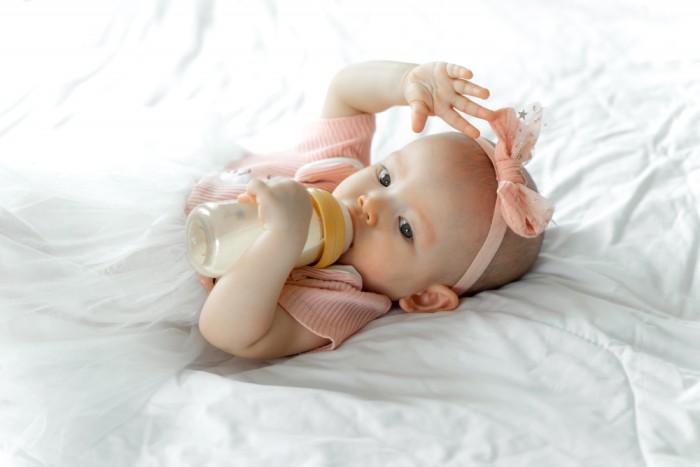 Young child lying on their back with a baby bottle in their mouth