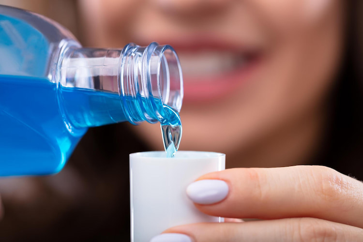 a close-up of a woman pouring mouthwash in the bottle cap.