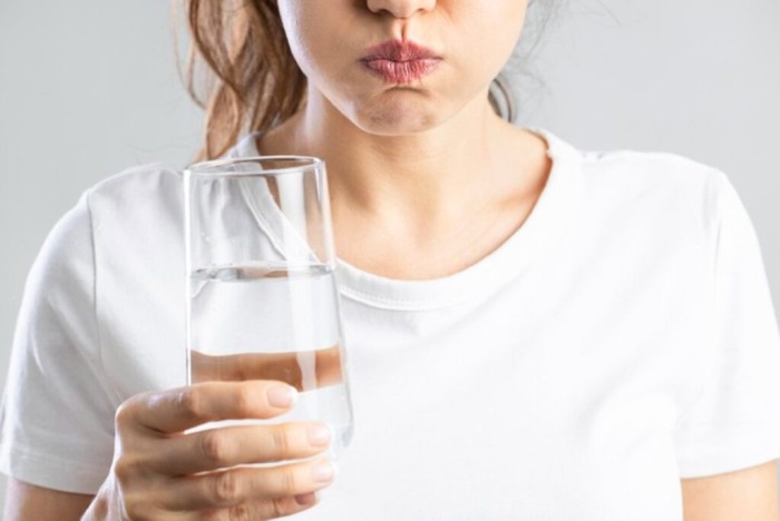 A woman is rinsing her mouth with water to prevent the pigmented food she just ate from negatively affecting her teeth whitening results.