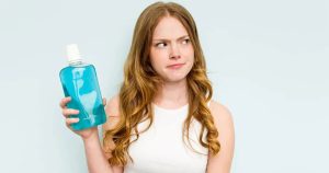 A young woman holding a mouthwash bottle in her hand with a hesitant look on her face.
