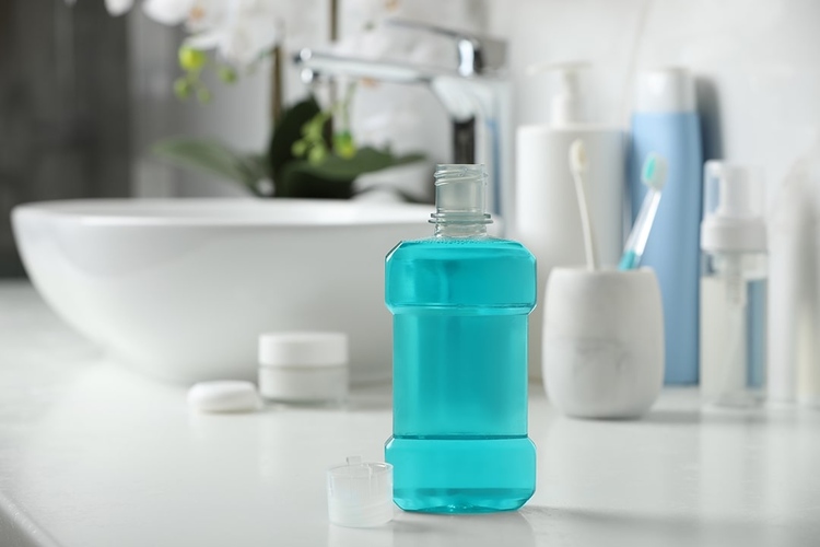 A bottle of mouthwash placed next to the sink with oral-care items in the background.