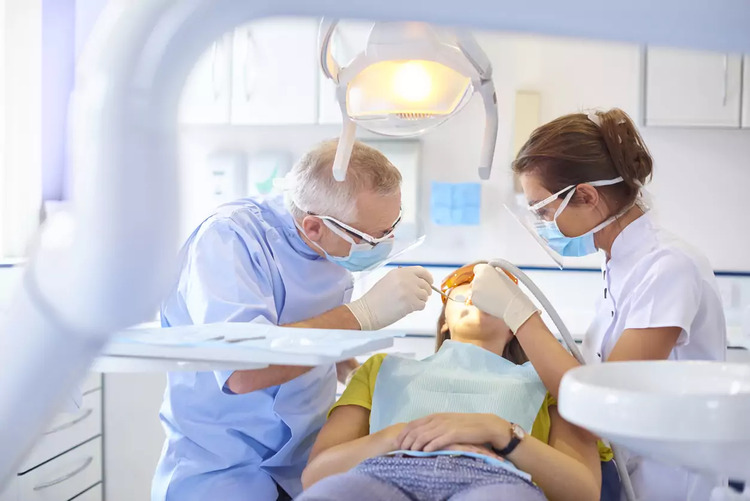A dentist, assisted by a dental nurse, performing a wisdom tooth extraction in the operating room.