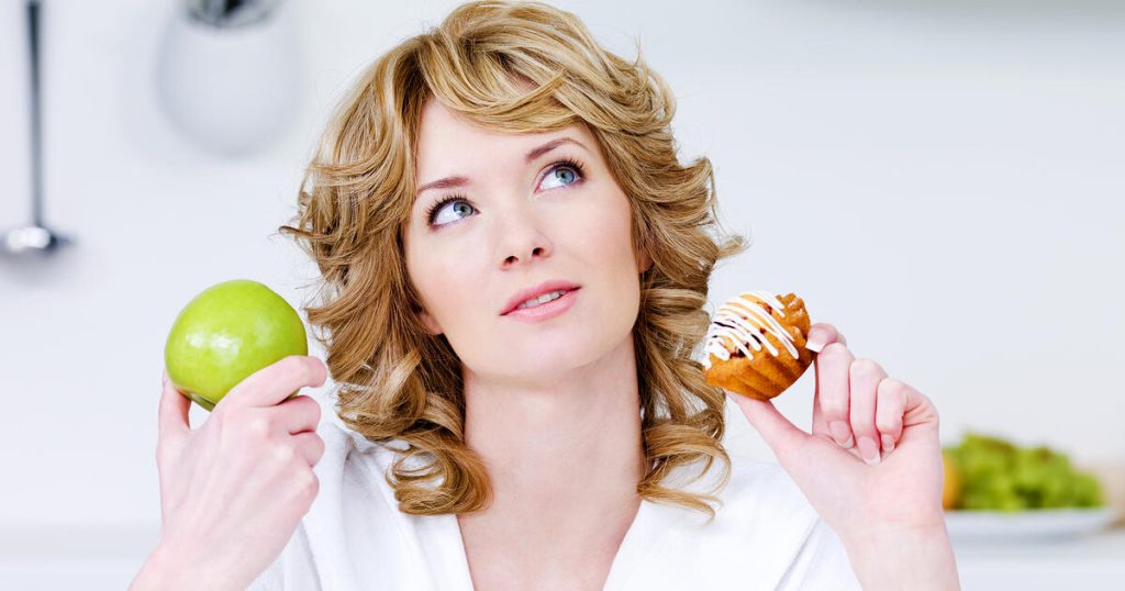 Young woman thoughtfully holding two different foods in her hands, deciding what to eat after root canal.