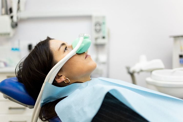 A young woman in a dental clinic receiving nitrous oxide sedation (laughing gas) to reduce dental phobia and anxiety during treatment.