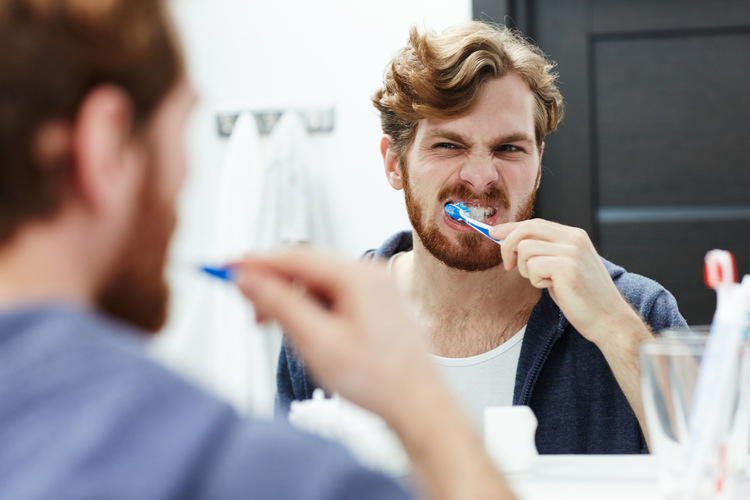 Young man brushing his teeth aggressively in front of the mirror