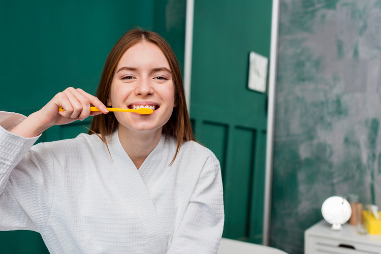 Young woman smiling at the camera while brushing her teeth