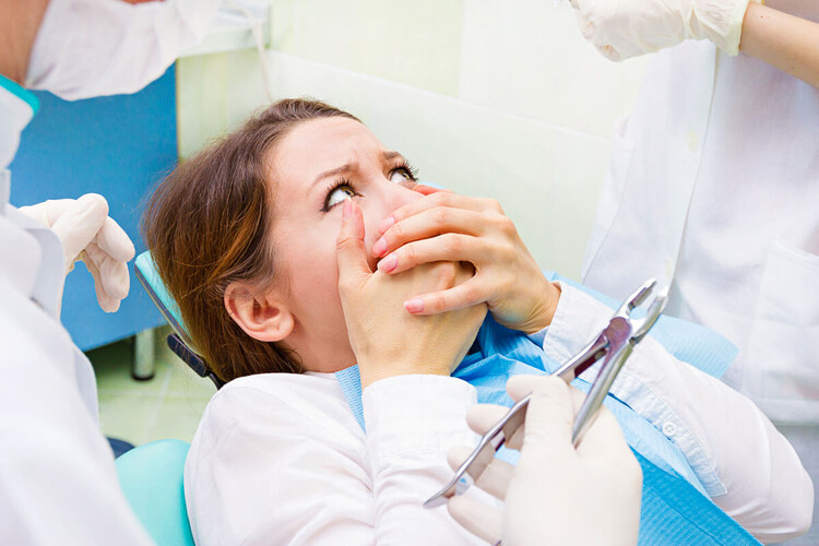 A woman sitting in a dental chair covering her mouth with her hand, showing dental phobia.