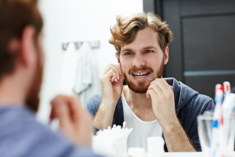 A young man flossing in front of a mirror to help extend the life of his dental crowns.