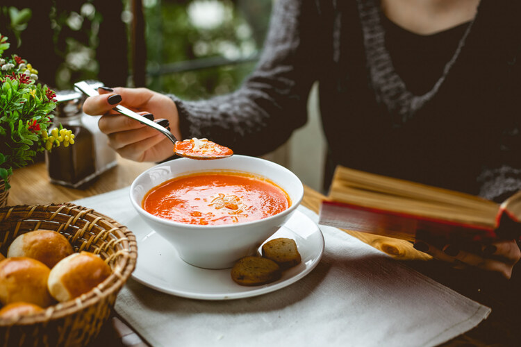 A bowl of soft food on a table with a woman sitting and eating during wisdom tooth extraction recovery