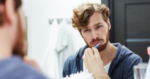 Young man brushing his teeth in front of the mirror with a frustrated expression
