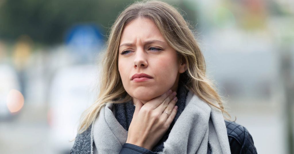 Young woman outdoors in cold weather holding her throat, experiencing dry mouth in Toronto.