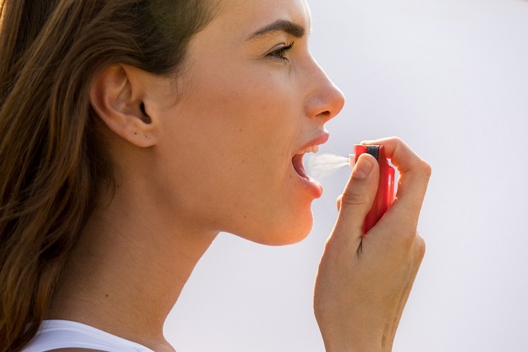 Woman using oral saliva spray to relieve dry mouth symptoms (xerostomia treatment)
