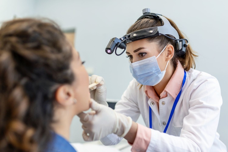 Dental hygienist examining a female patient’s mouth for dry mouth symptoms in a dental clinic