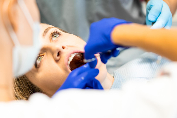Close-up of a young woman in a dental clinic having tooth extraction by her dentist.