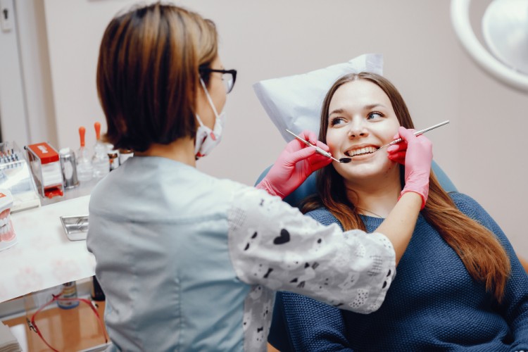 a young woman sitting in a dental chair receiving professional dental cleaning from a dental hygienist to help prevent loose gum flap between teeth.