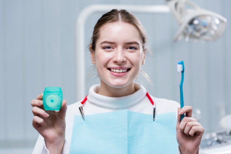 Young woman holding a toothbrush in one hand and dental floss in the other for maintaining oral hygiene to prevent tooth abscess