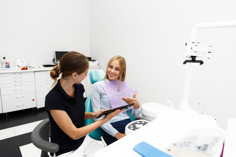 A young woman sitting in a dental chair discussing her dental condition with a dental hygienist before a cleaning procedure.