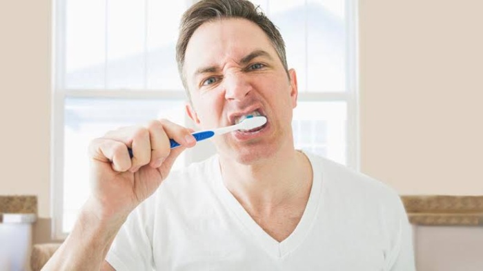 A man aggressively brushing his teeth while facing the camera.