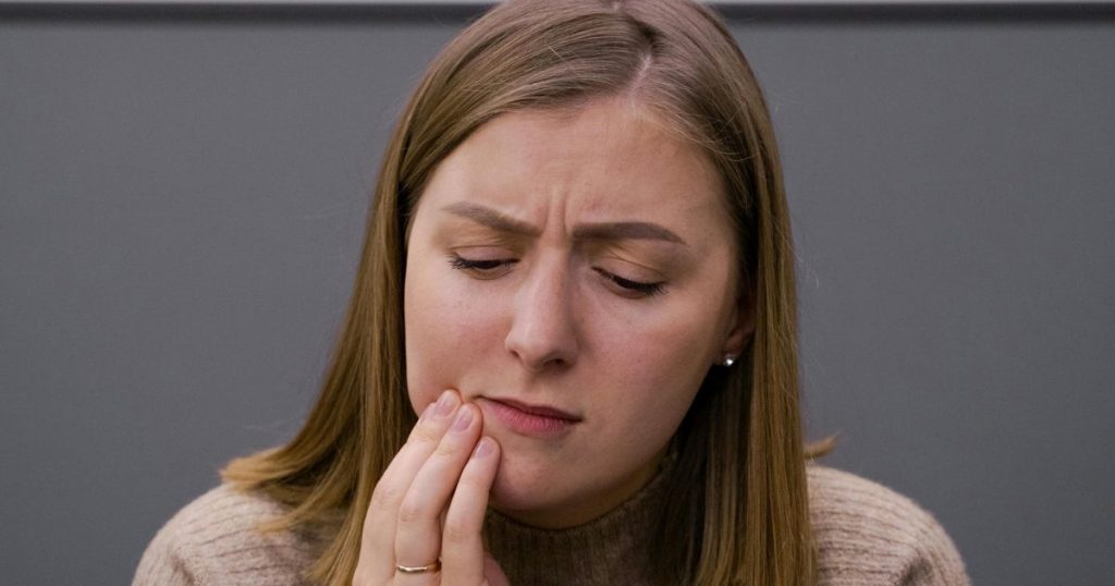 Woman with her hand on her jaw and cheek, thinking about how long does dental numbing lasts?
