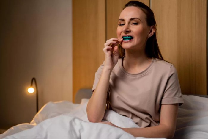 A woman lying in bed with a colored night guard in her mouth.