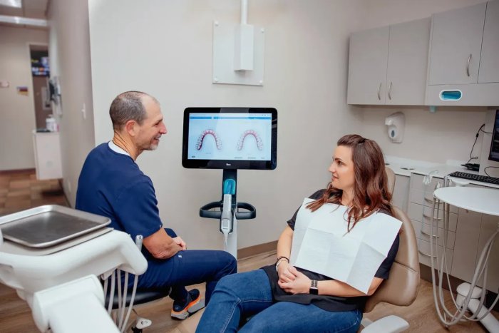 A dentist in the clinic reviewing a female patient’s dental X-rays with her present to determine the best night guard for teeth grinding.