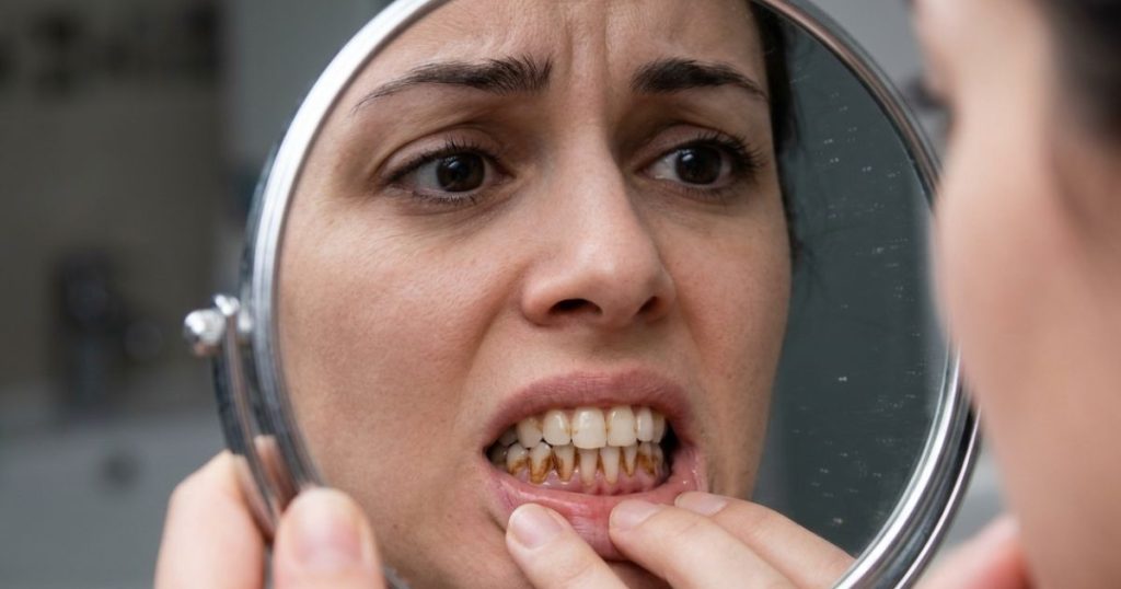 A worried woman looking in the mirror, inspecting brown stains on teeth